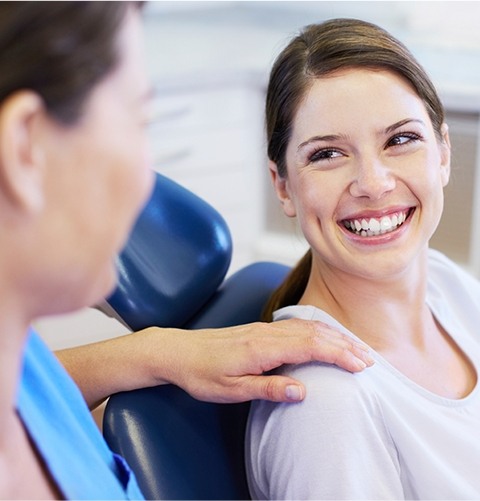 Woman in dental chair smiling at dental team member