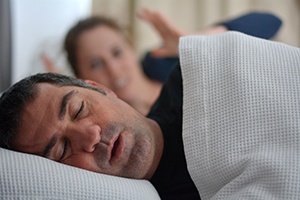 Man snoring, frustrated wife in background