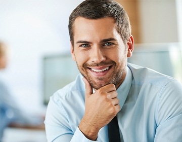 Man in dress shirt and tie smiling while resting chin in hand