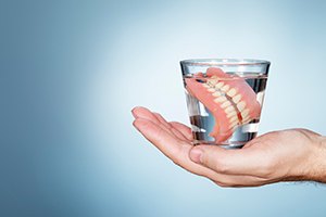 Dentures in glass of water, resting on hand