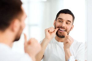 Man in white shirt flossing teeth in front of mirror