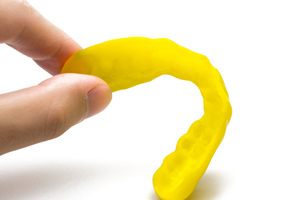 Fingers picking up yellow mouthguard against white background