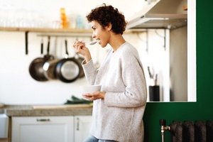 Woman standing in kitchen, enjoying yogurt after oral surgery
