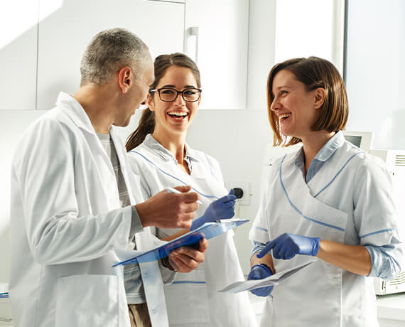 Three dental team members with clipboards talking in dental office