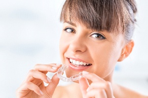 Young woman with brown hair holding Invisalign aligner