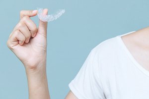 Person in white shirt holding Invisalign aligner against neutral background