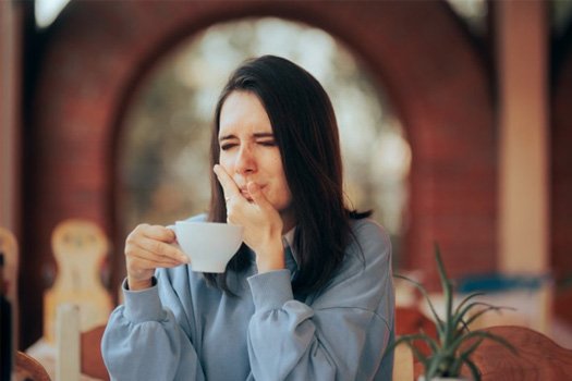 Woman holding her jaw after sipping a hot drink