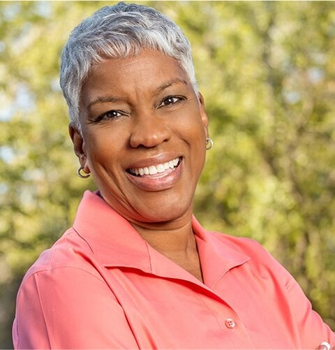 Older woman in salmon colored blouse smiling outdoors