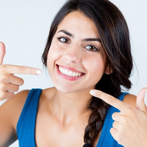 Woman pointing at her teeth after smile makeover in Belmont