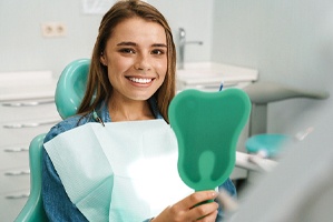 Dental patient using mirror to admire results of cosmetic dentistry service