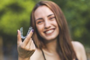 Happy woman holding aligner for Invisalign in Belmont