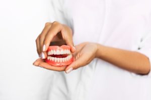 Manicured hands holding dentures, which can affect taste