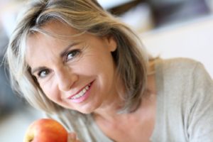 Senior woman enjoying apple with the help of implant dentures