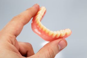 Thumb and forefinger holding lower denture