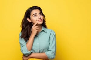 Woman standing against yellow background, wearing curious expression