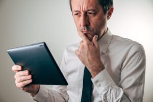Man touching his mouth while reading information on his tablet 